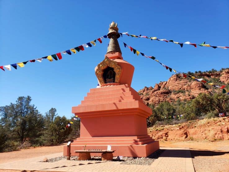 Tall terracotta monument in the desert with prayer flags attached