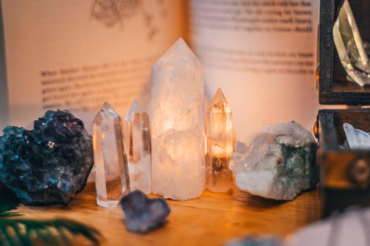 Several crystals including clear quartz and selenite pillars stand upright against an open book and a box