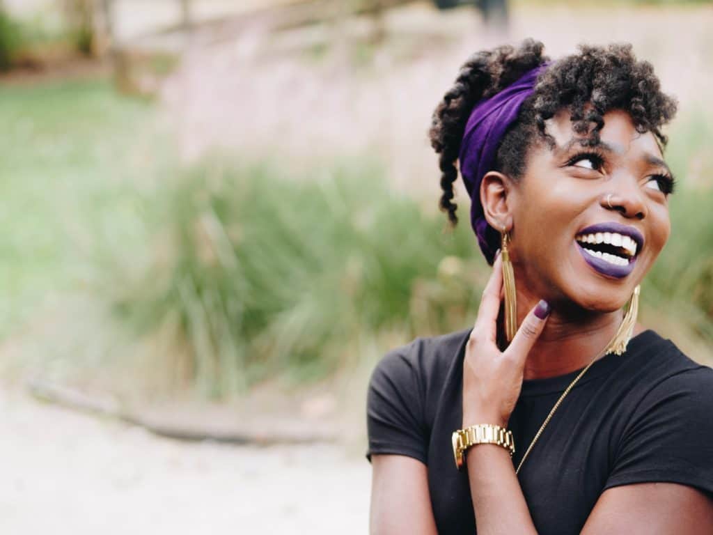 A woman touches her neck softly while grinning.