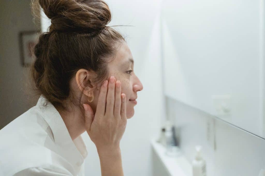 A woman touches her face and looks in the mirror.