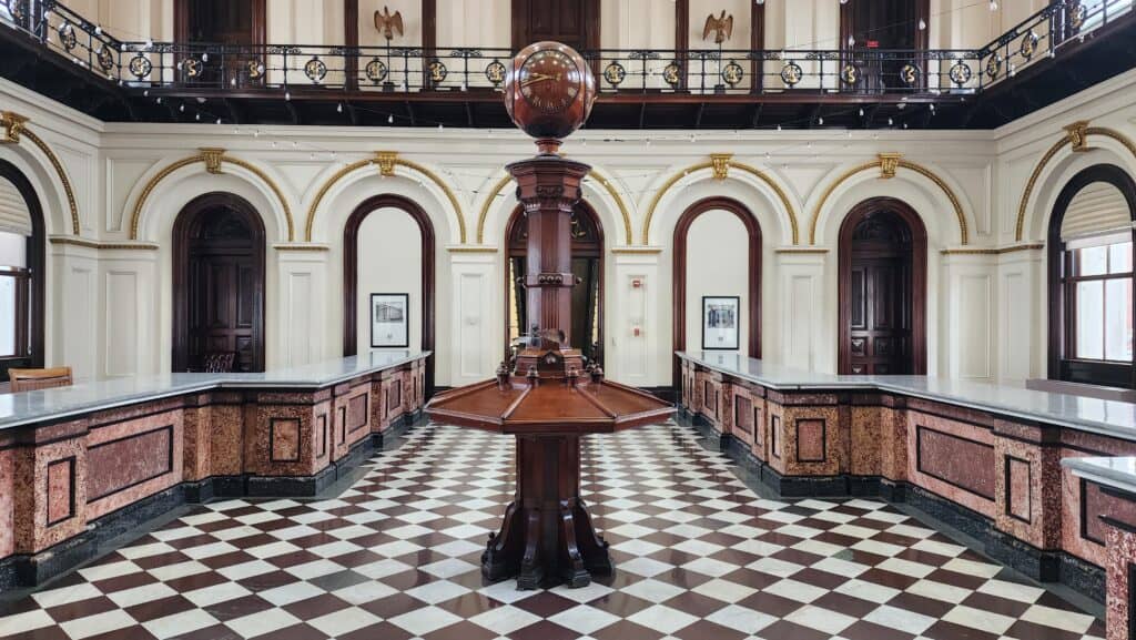 A wooden clock stands in teh center of an old building.