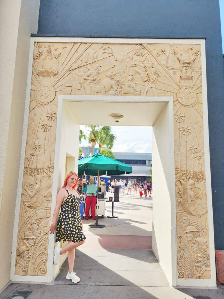 A woman poses in an archway with art deco designs carved into it.