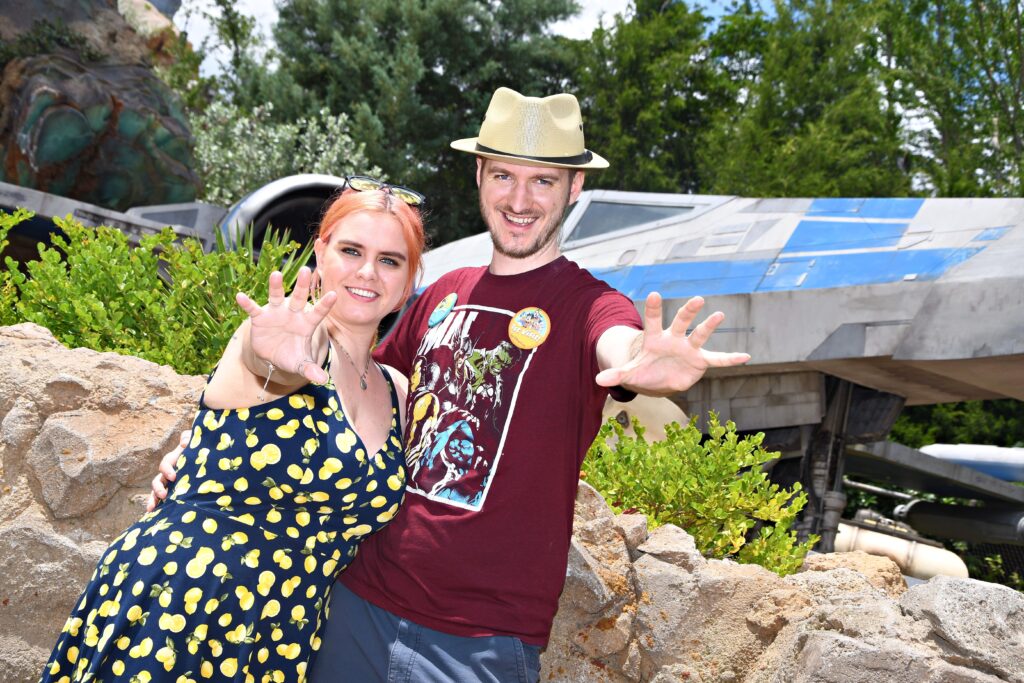 A woman and a man pose in front of a sci-fi ship.