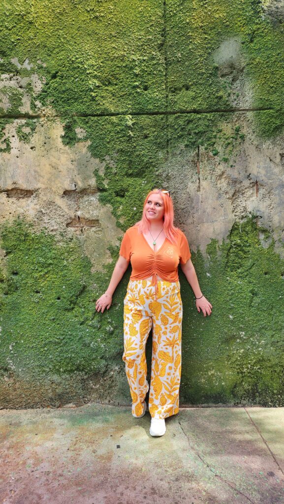 A woman stands in front of a moss covered wall.