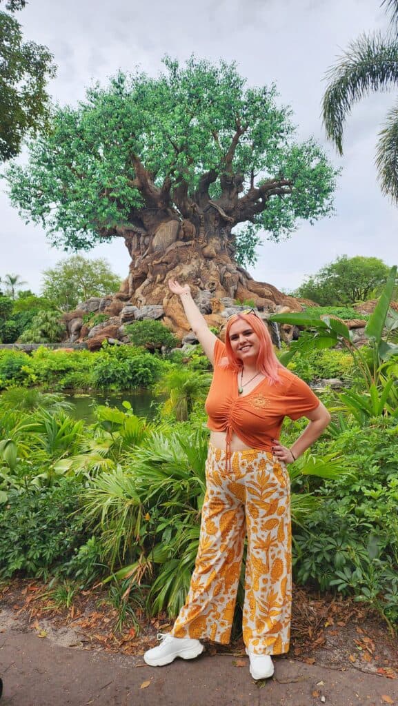 A woman stands in front of a lagoon and a large tree sits across the water.