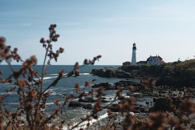 A lighthouse in the distance standing above the ocean on a rocky cliff.