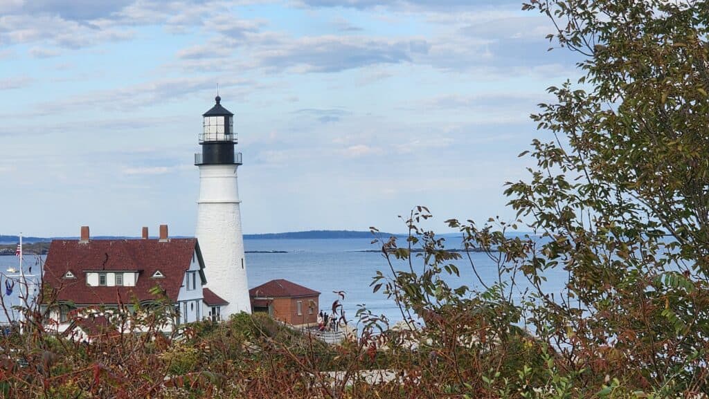 A lighthouse and boarder house next to a calm ocean.