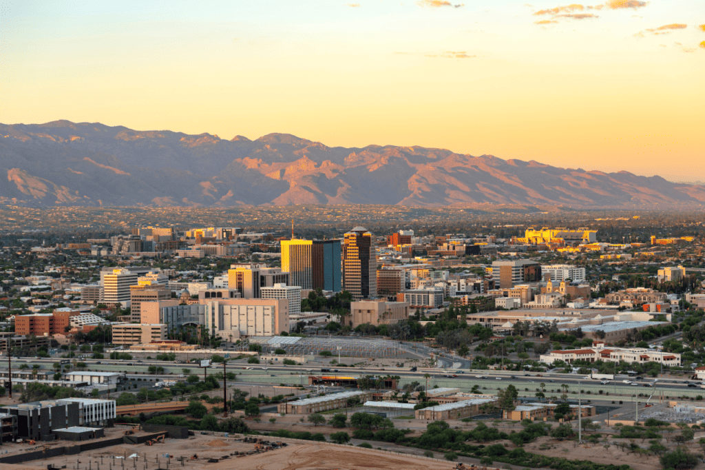 The skyline of a small city with a few tall buildings, set up against mountains, beneath a hazy sky.