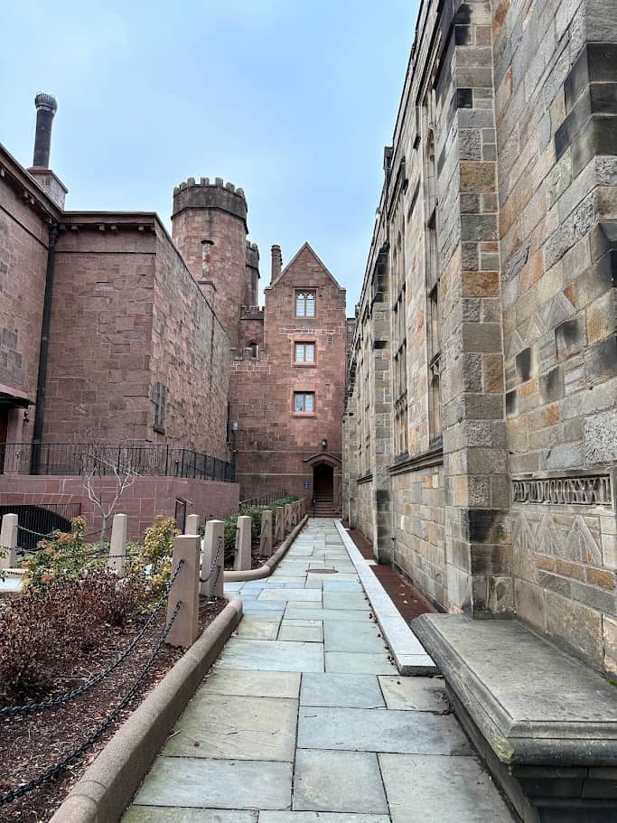 Medieval looking brick buildings tower over a paved path.