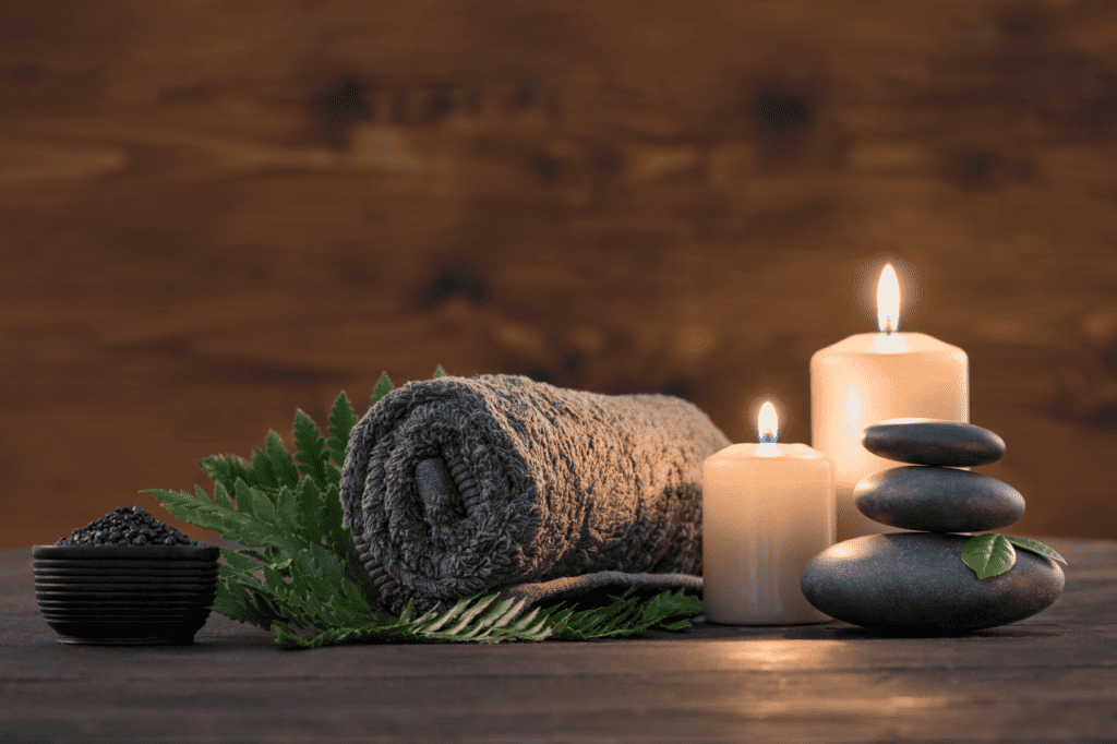 A towel and massage stones are placed next to lit candles.