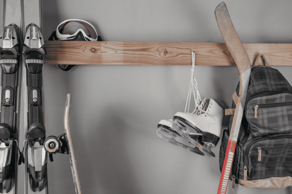 Skis, ice skates, a hockey stick, and a backpack are hung on a rack.