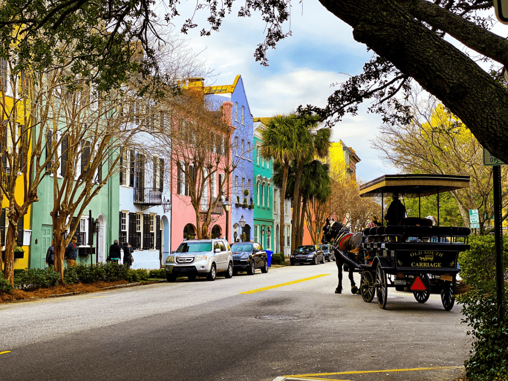 A city street with colorful homes in oranges, pinks, greens, blues, and purples. A horse drawn carriage is parked on the side of the road.