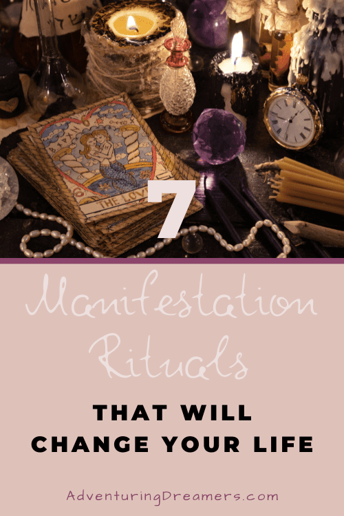 A table is crowded with various items including candles, pearls, perfume bottles and tarot cards. Text below the image reads "7 manifestation rituals that will change your life. Adventuringdreamers.com"