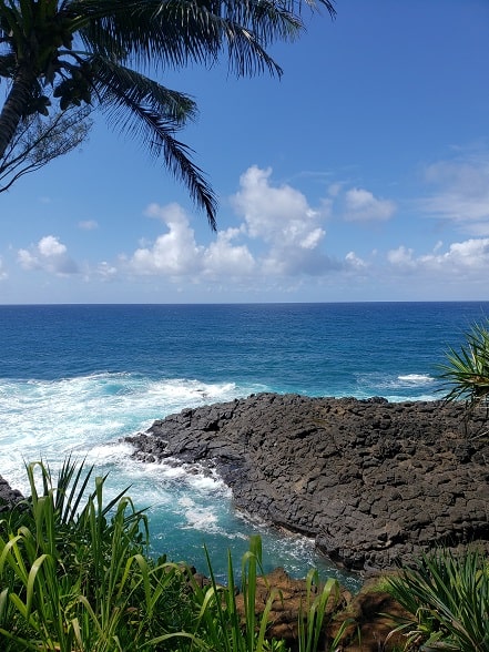 A view of the ocean beyond a peninsula of igneous rocks on the edge of a tropical island.