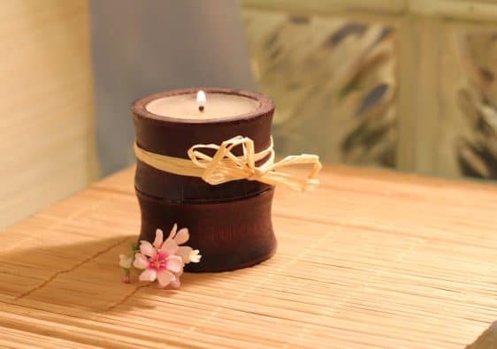 A candle on a bamboo table with a pink flower next to it.