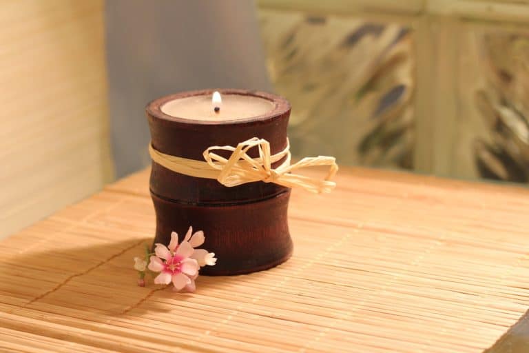 A candle on a bamboo table with a pink flower next to it.