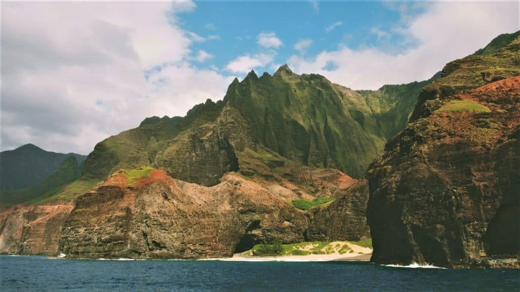 A jagged mountain covered in green lush protrudes from the coast of an island.