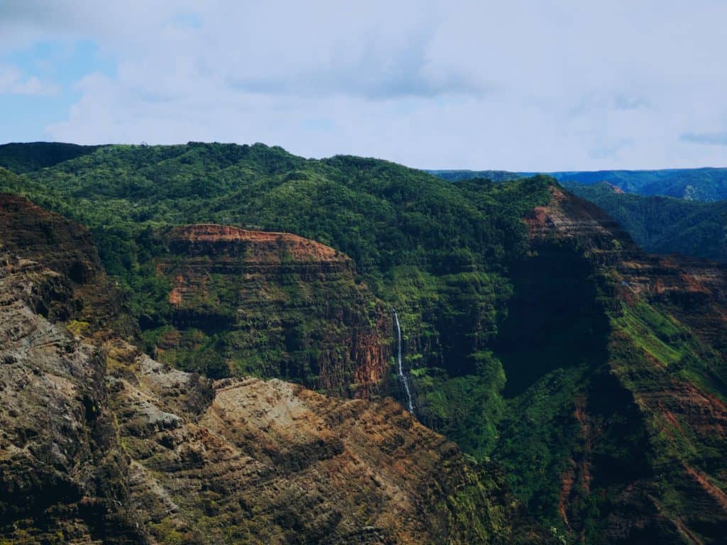 A lush, green mountainous region with a sliver of a waterfall trickling down the tall mountain walls.