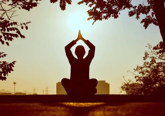 Silhouette of a person meditating with their arms raised above their head