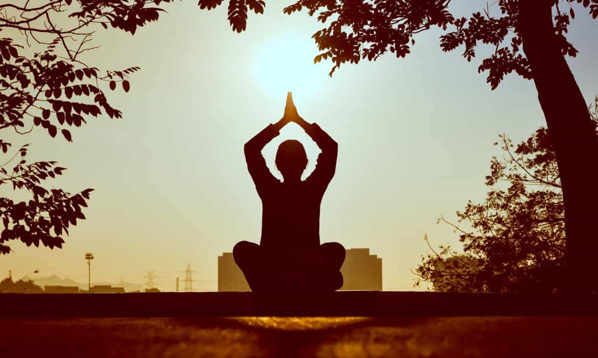 Silhouette of a person meditating with their arms raised above their head