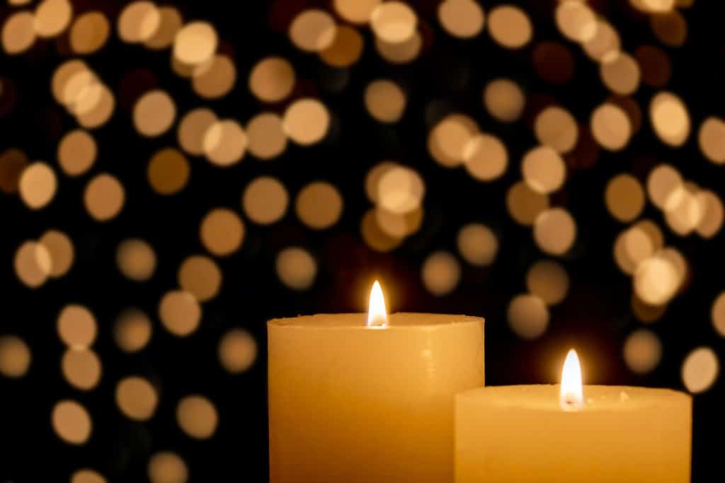 Two lit cream-colored candles with gold sparkles in the background.