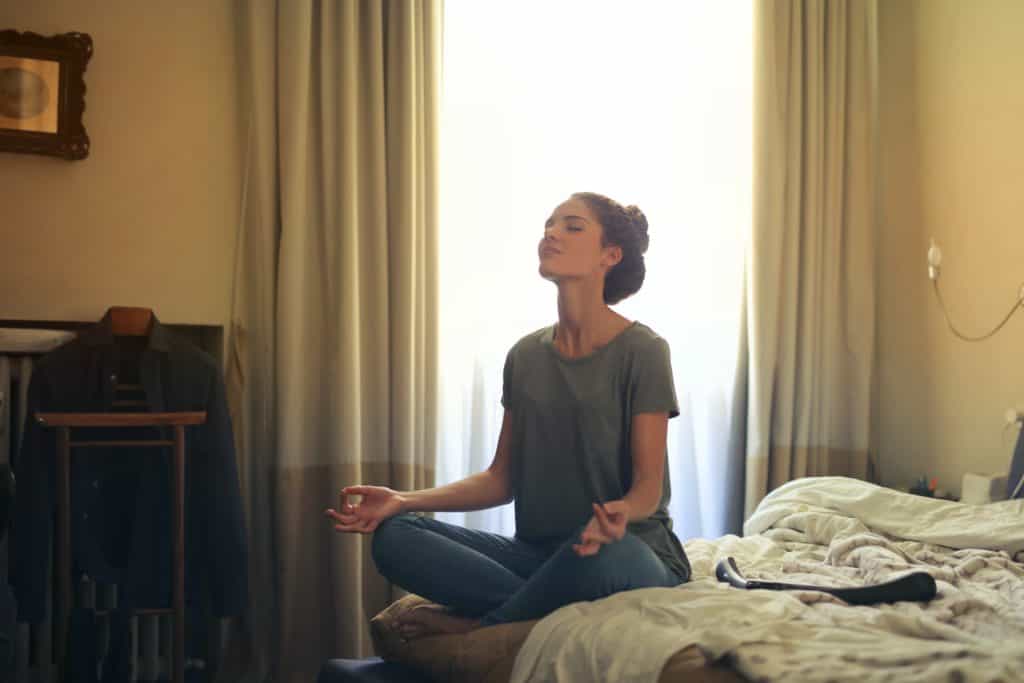 A woman meditates on her bed.