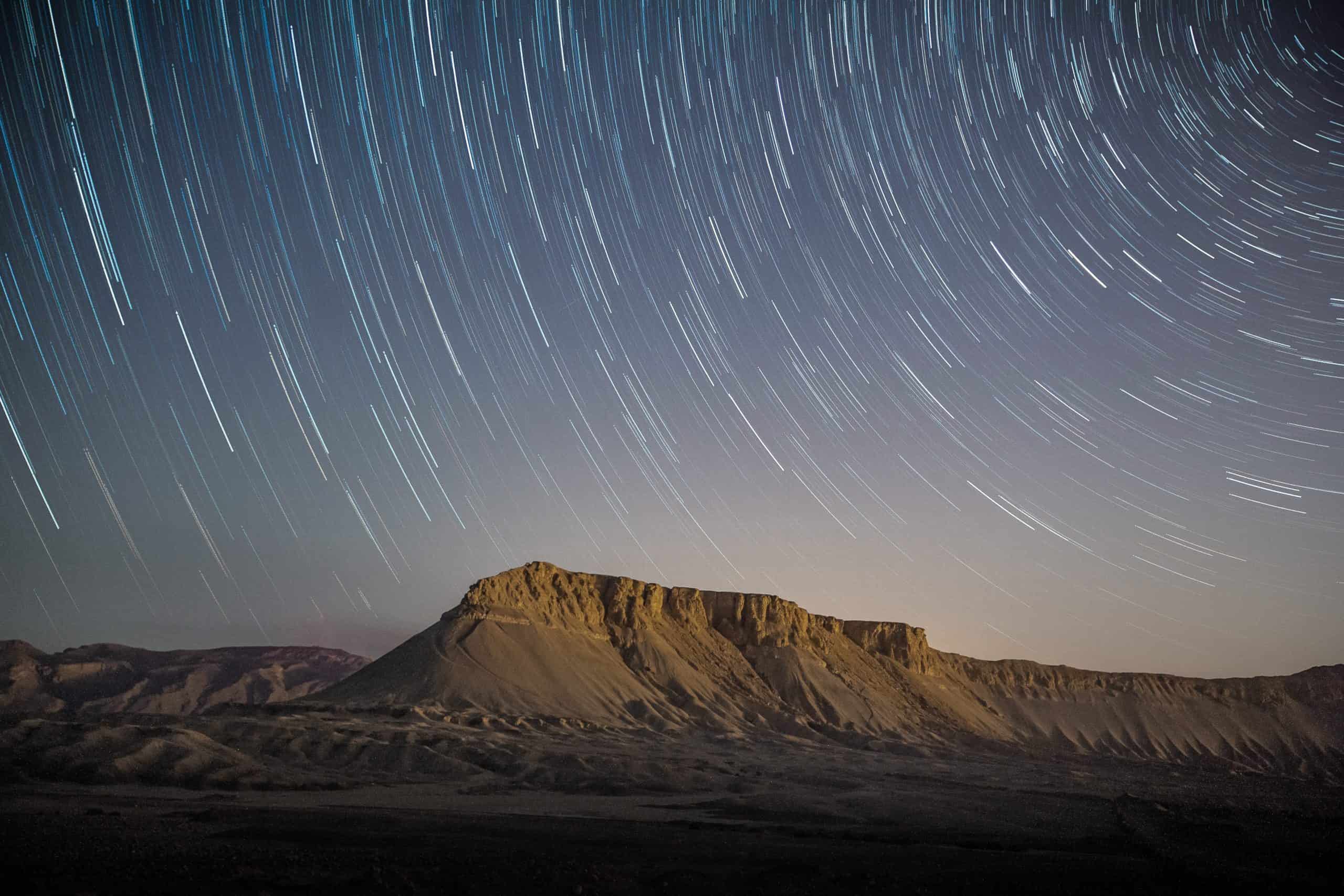 A desert mountain under a sky full of swirling stars
