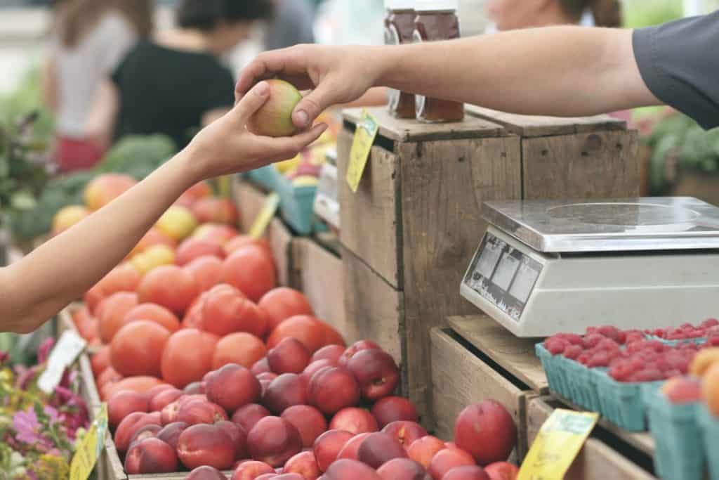 An arm reaches out for an apple that is being handed over a register in a produce section.