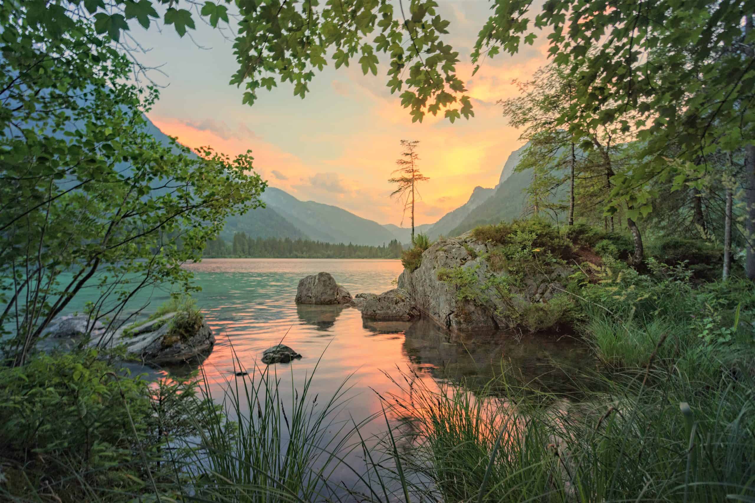 A serene lake at sunset surrounded by green trees.