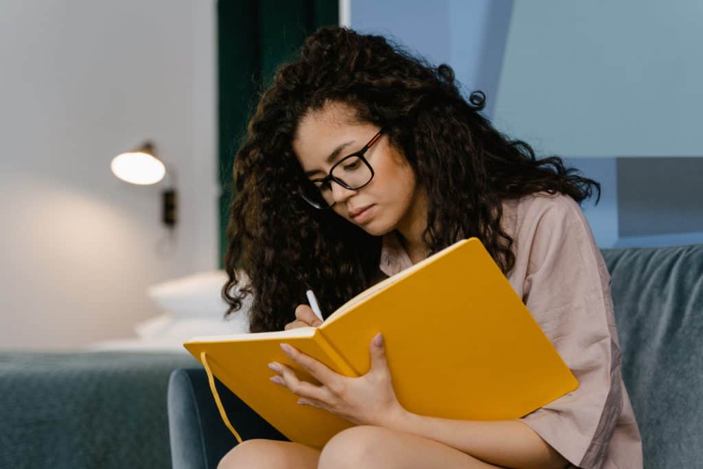 A woman journals on a couch.