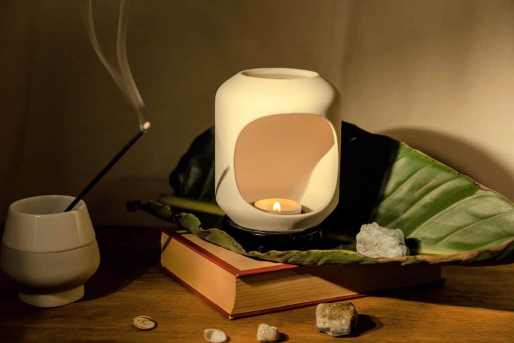 A table holding a candle inside a candle melt holder, incense in a cup, a book, and crystals.