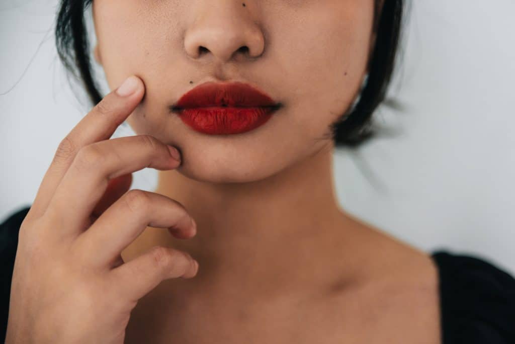 A woman with bright red lips touches her face