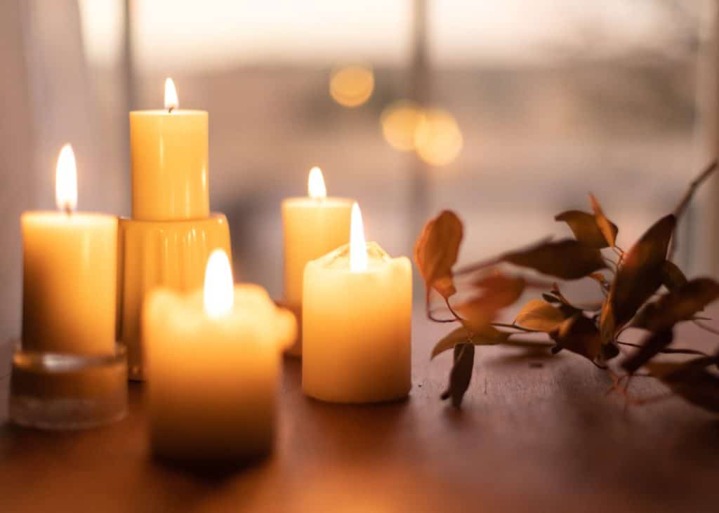 Assorted sized white candles on a table next to fall leaves.