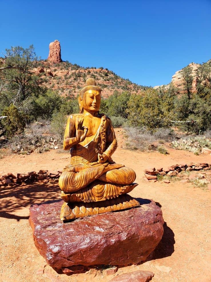 A Buddha statue perched on top of a red rock.