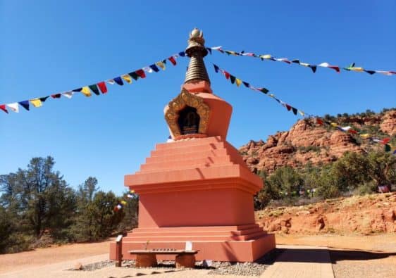 Tall terracotta monument in the desert with prayer flags attached