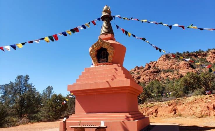 Tall terracotta monument in the desert with prayer flags attached