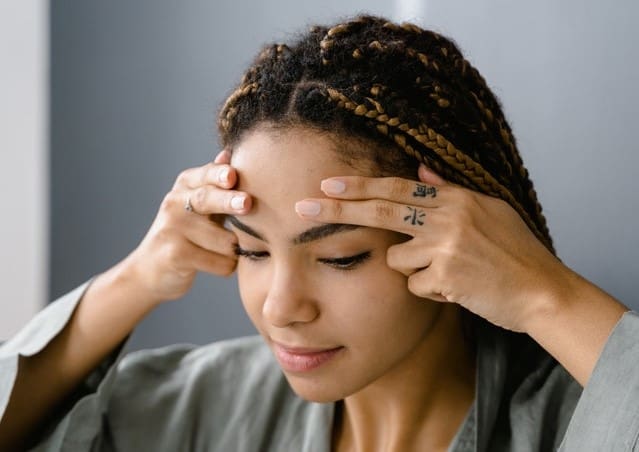 A woman touches her face above the eyebrows