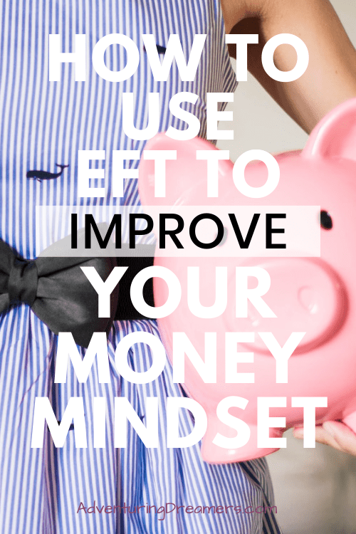 A woman in a blue dress holds an overly large pink piggy bank. Text overlay reads: How to use EFT to improve your money mindset.