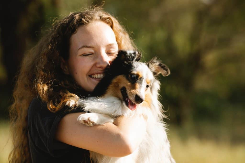A woman grins and tightly cuddles a puppy.