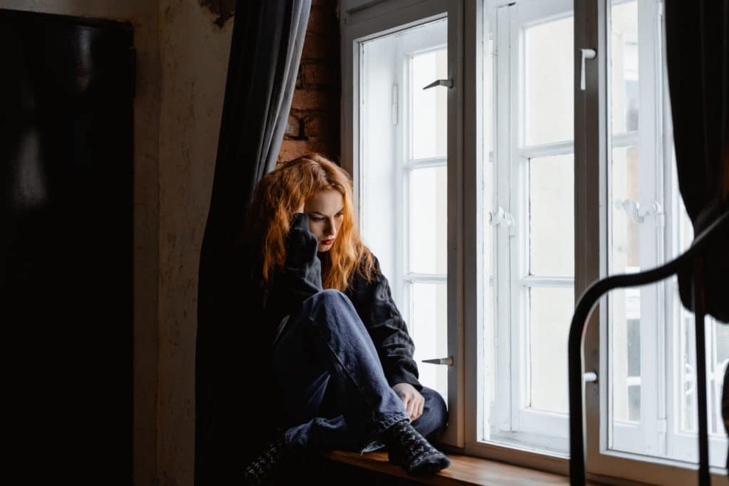 A woman sits on a window seat looking distraught.