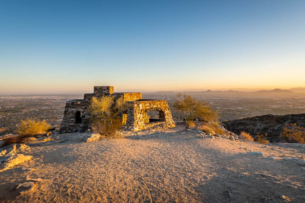 A stone structure stands alone overlooking a city in the distance.