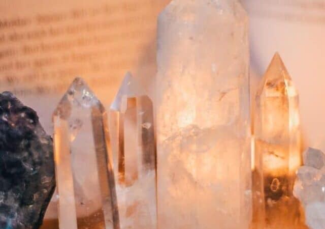 Several crystals including clear quartz and selenite pillars stand upright against an open book and a box