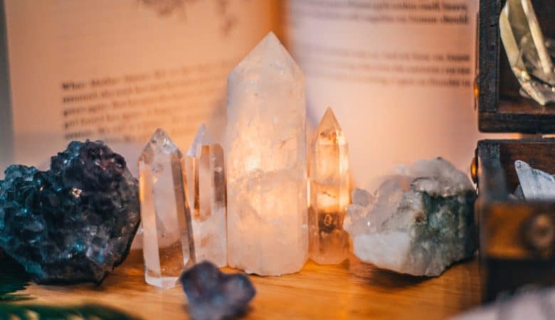 Several crystals including clear quartz and selenite pillars stand upright against an open book and a box