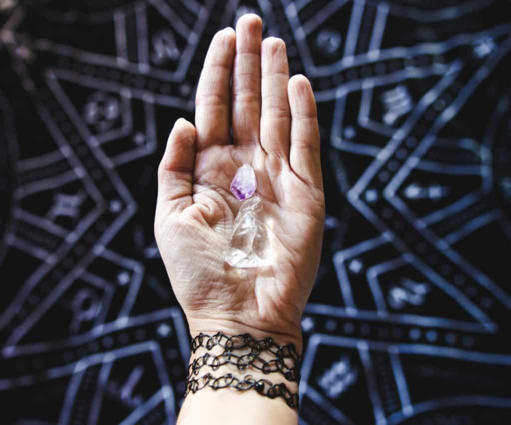 An open palm holds an amethyst and clear quartz.