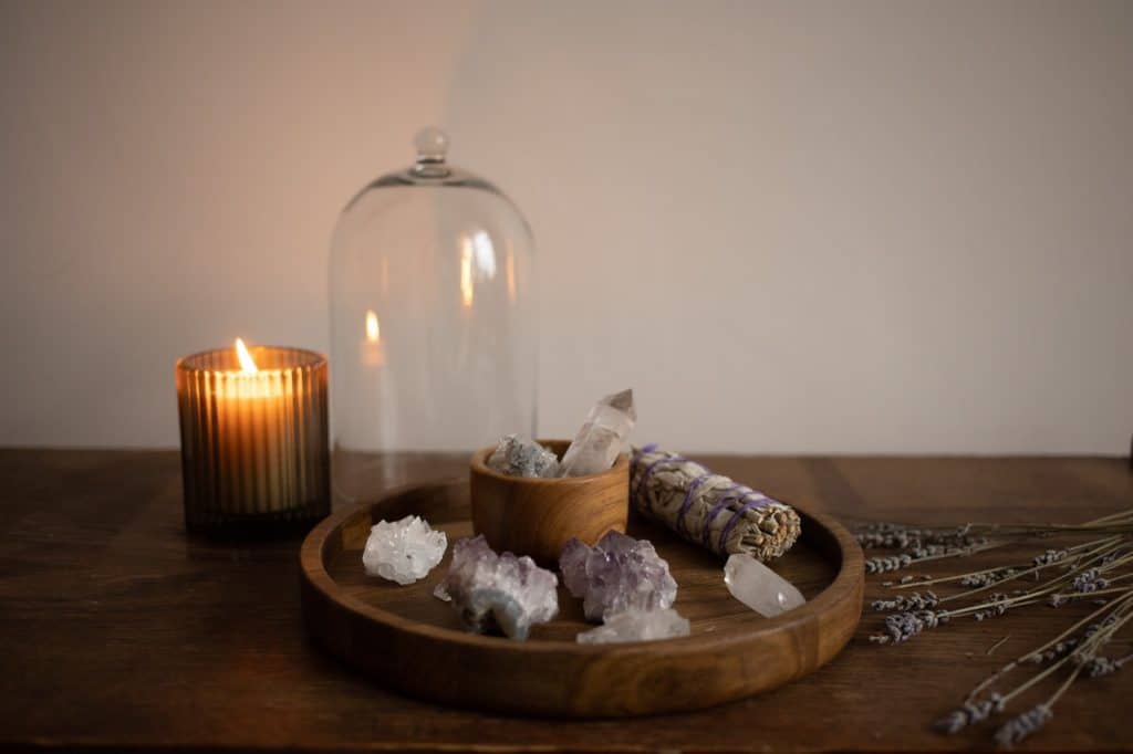A tray table holds a mixture of stones and sage next to a lit candle and a lavender sprig.