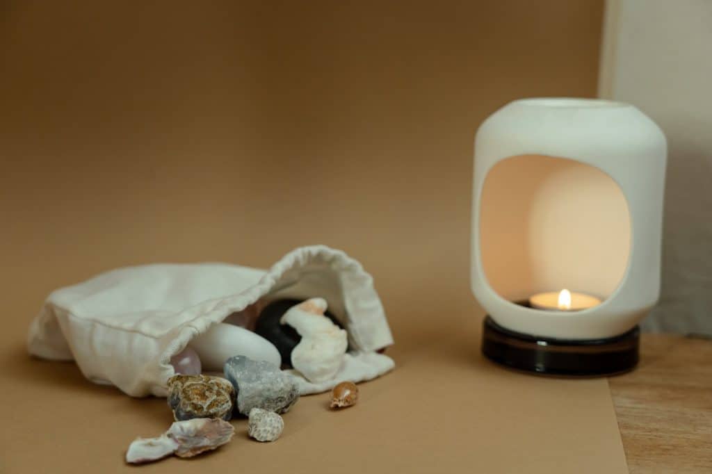 A bag of crystals and stones is spilling out on a table next to a lit tea light.
