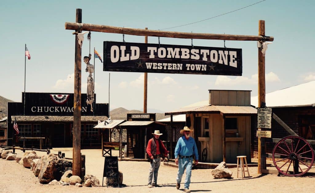Two cowboys walk under a wooden post sign that says, "Old Tombstone Western Town."