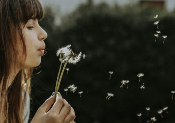 A woman blows the seeds of a dandelion flower.