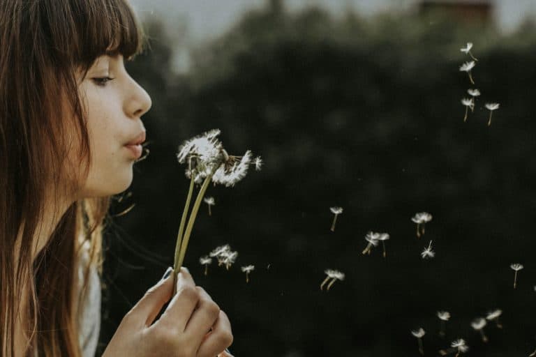 A woman blows the seeds of a dandelion flower.