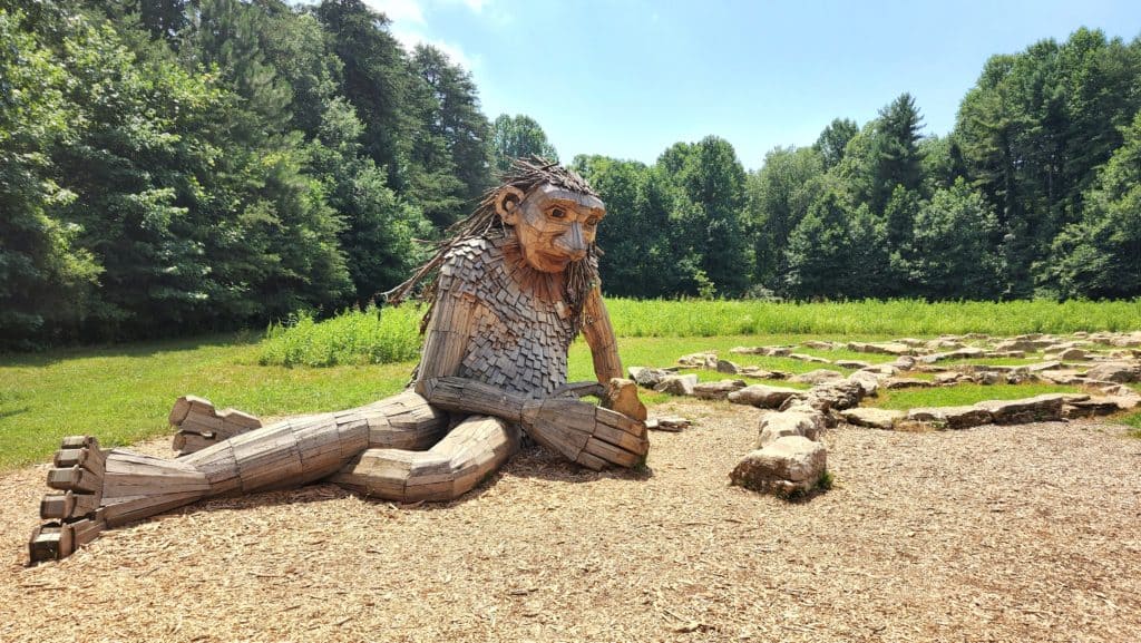 A giant wooden sculpture of a troll playing with rocks.